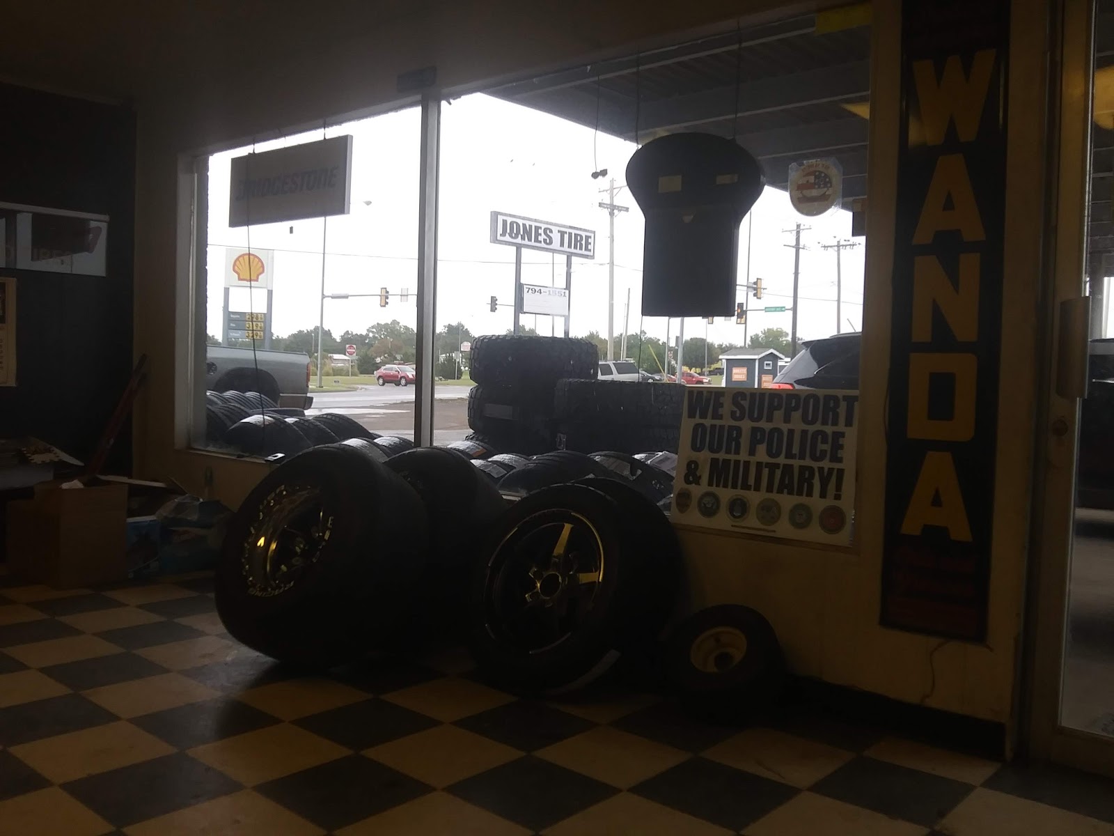 Front window of Jones Tire with the roadside sign visible and custom wheels on the checkered floor